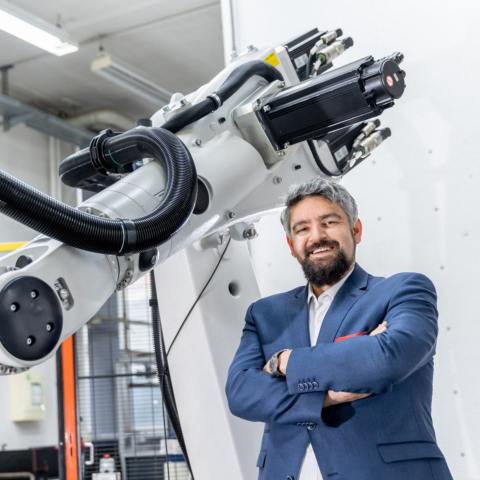 Jun. Prof. Andreas Wortmann vor einem Roboter am Institut für Steuerungstechnik der Werkzeugmaschinen und Fertigungseinrichtungen (ISW).