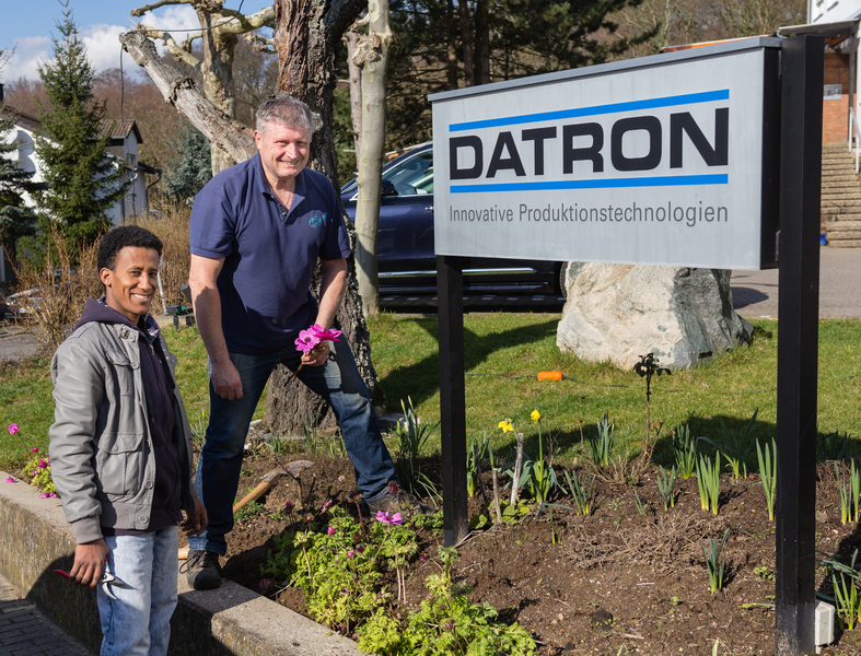 Johannes Stork, Mitarbeiter im Gebäudemanagement und der neue Mitarbeiter Aaron Arefe Mesegna aus Eritrea arbeiten bei der DATRON AG im Garten.
